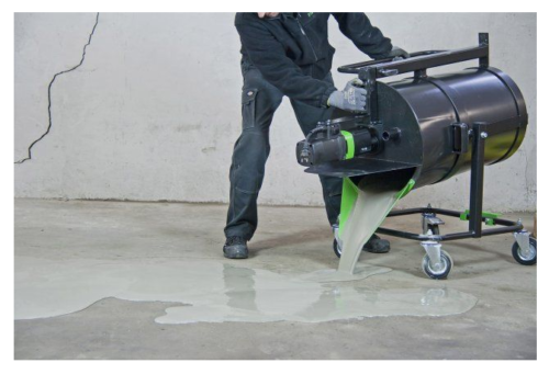 A person in dark clothing operates a machine that is pouring a liquid substance onto a concrete floor.